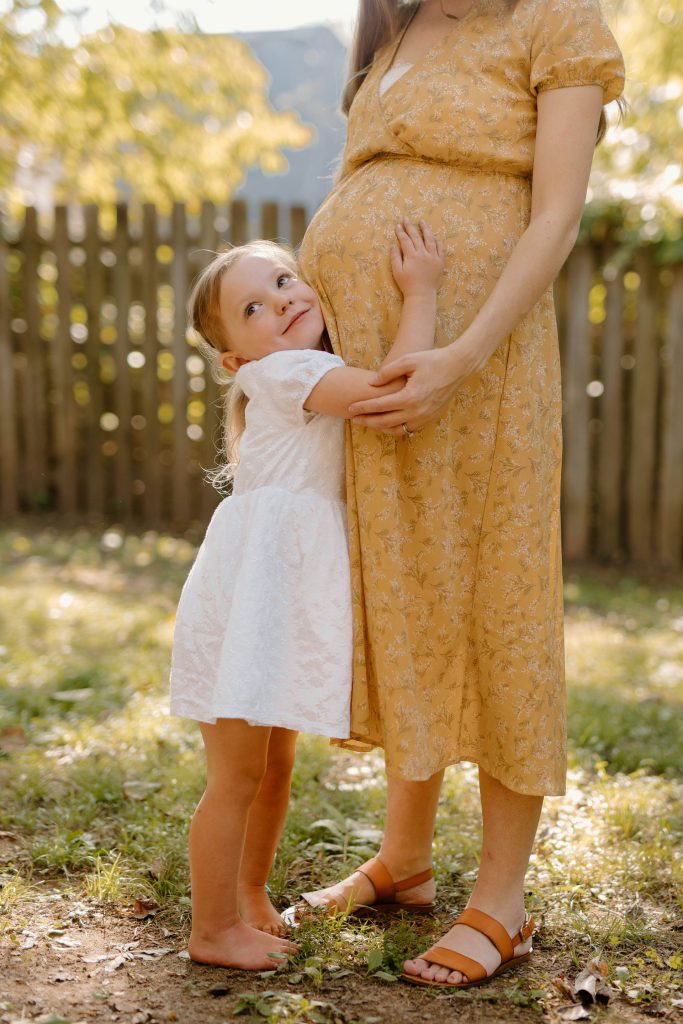 Kleines Mädchen, das ihre schwangere Mutter umarmt